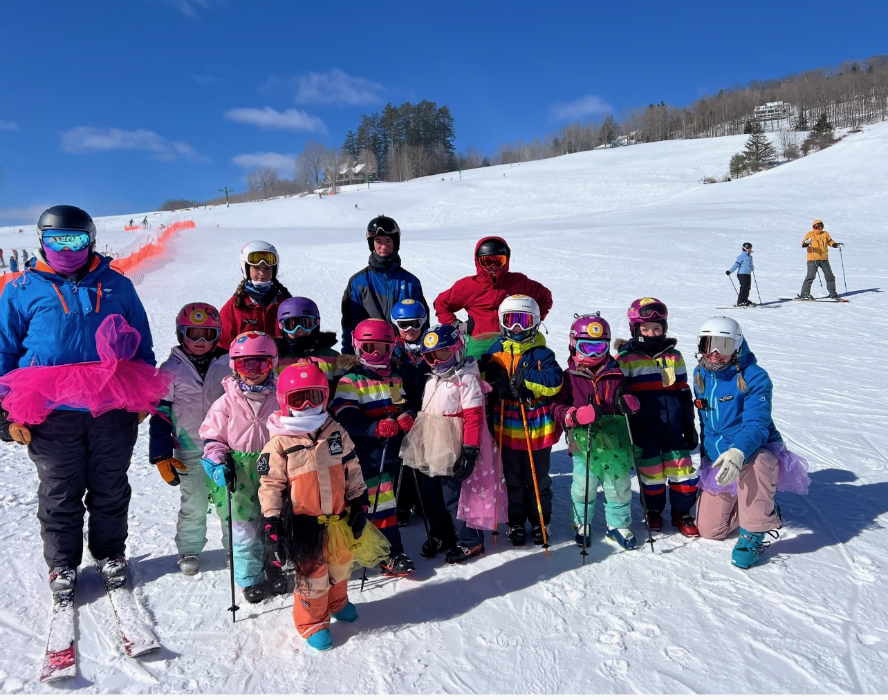 Ski instructors and skiers all wearing tutus on a sunny day with a blue sky behind them.